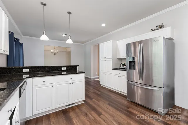 a kitchen with granite countertop a refrigerator a sink and white cabinets