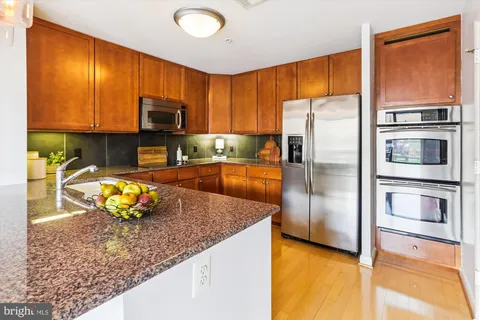 a kitchen with stainless steel appliances granite countertop a refrigerator a stove and a sink with wooden floor