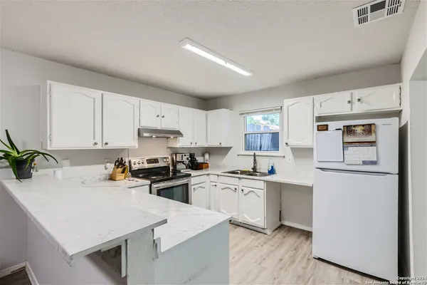 a kitchen with a sink a stove a refrigerator and white cabinets