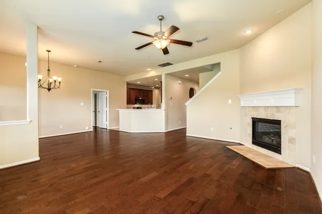 wooden floor in an empty room with a fireplace and a ceiling fan