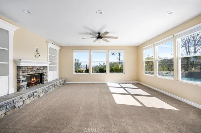 a view of a livingroom with a fireplace a ceiling fan and a kitchen view