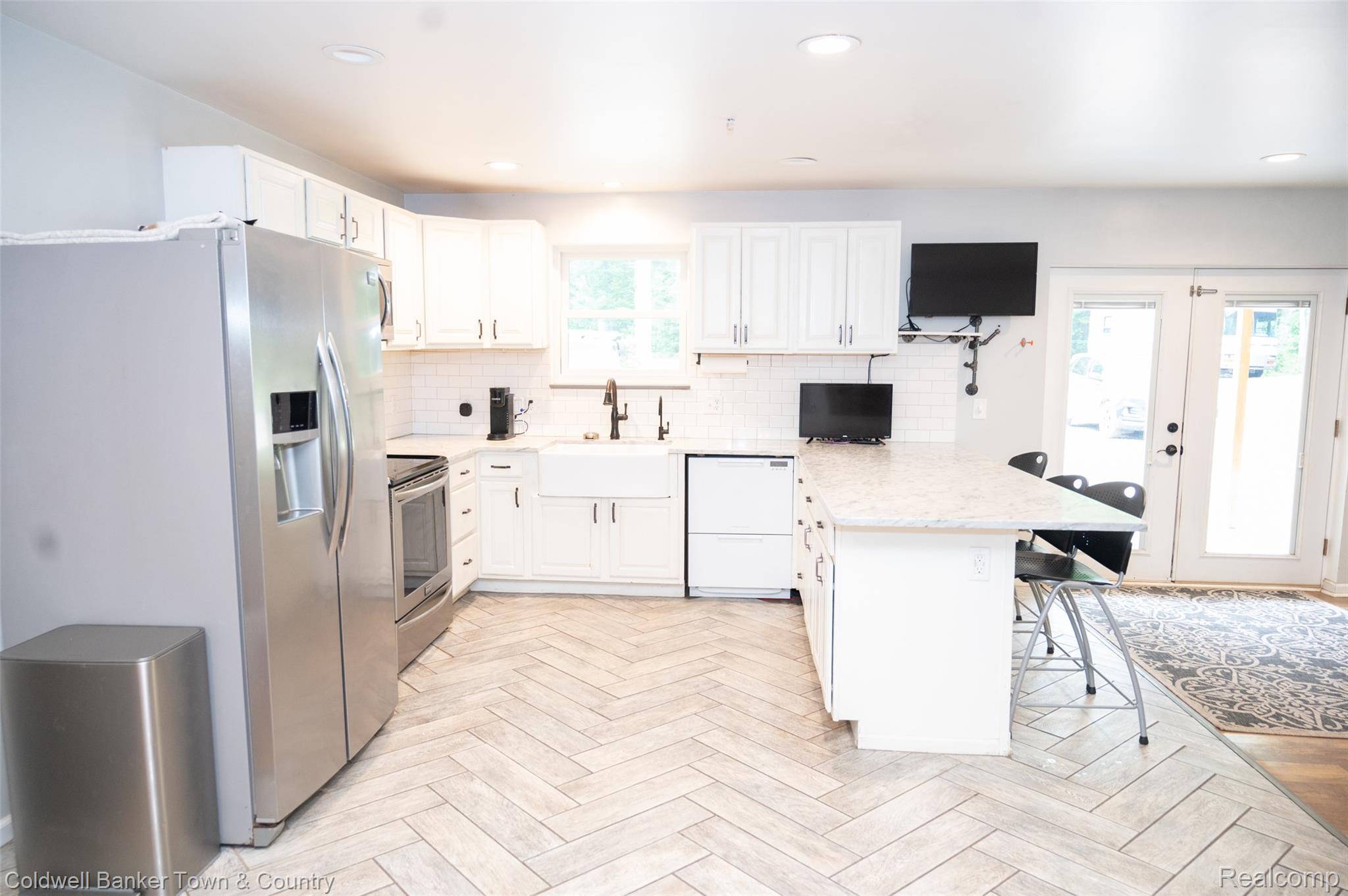 6150 North Fleming Road Howell, MI 48855 - Photo 9 of 23 Kitchen featuring light wood-finish flooring in a herringbone pattern, white shaker cabinetry, stainless steel appliances, and a central island with countertop seating