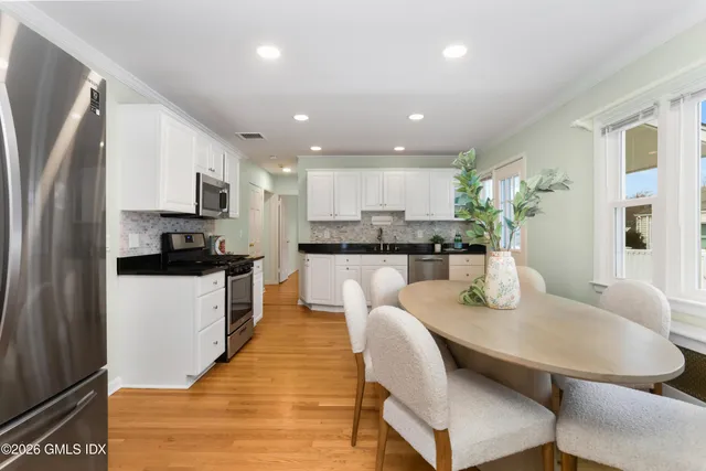 a kitchen with stainless steel appliances granite countertop a refrigerator a stove top oven a sink dishwasher and white cabinets with wooden floor