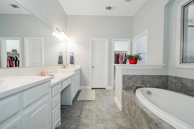 a en suite bathroom with a granite countertop double vanity sink a mirror and bathtub