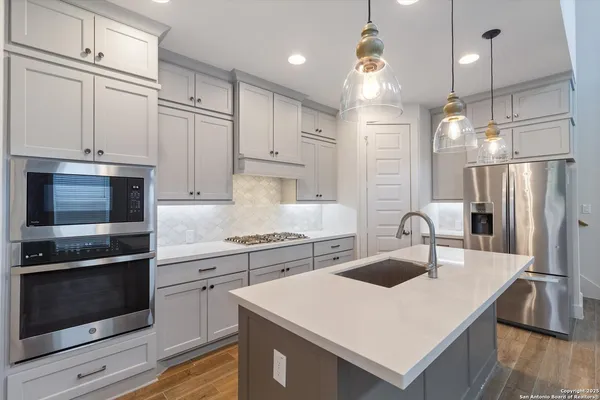 a kitchen with stainless steel appliances a sink a stove a refrigerator cabinets and chairs