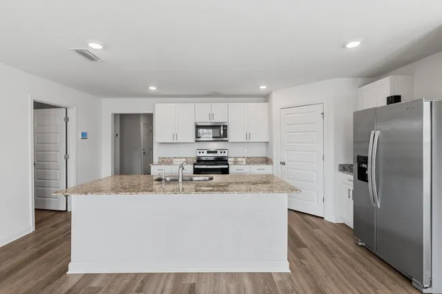 a large kitchen with stainless steel appliances granite countertop a stove a refrigerator a sink and dishwasher with wooden floor