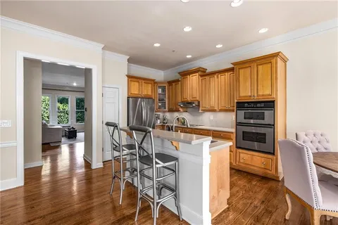 a kitchen with stainless steel appliances granite countertop a stove top oven a refrigerator a dining table and chairs with wooden floor