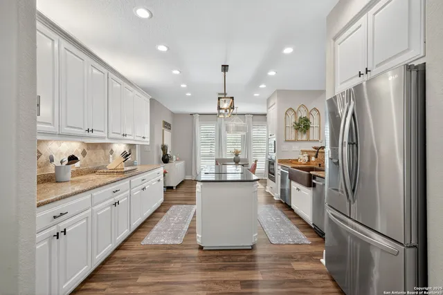 a kitchen with granite countertop a refrigerator a sink dishwasher and white cabinets with wooden floor