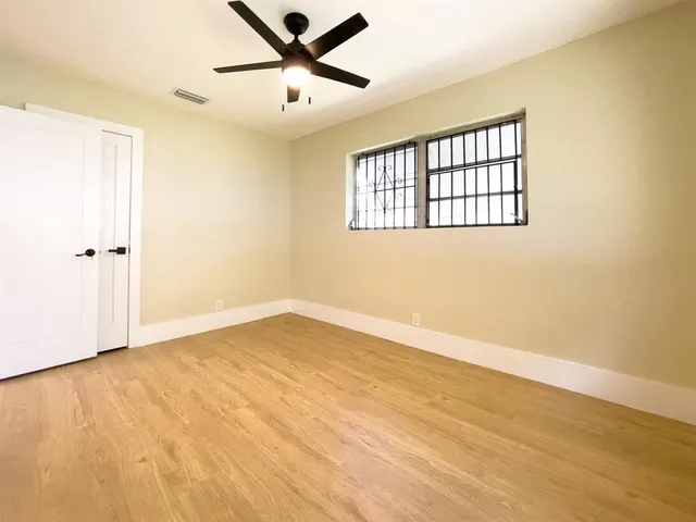 an empty room with wooden floor fan and windows