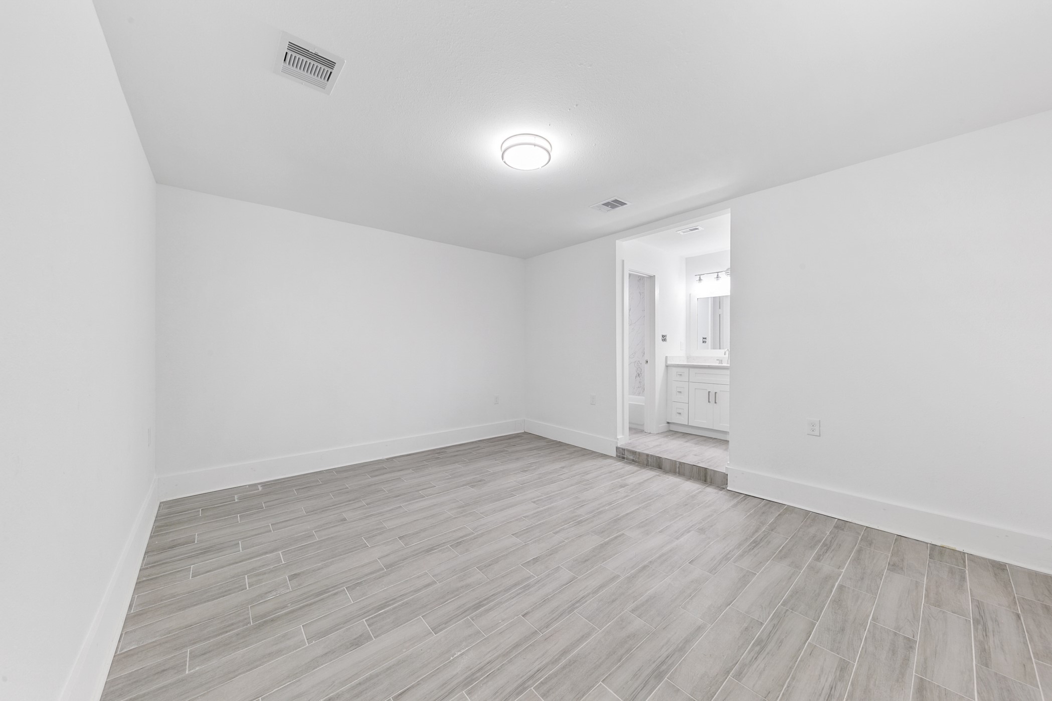 6811 McCullum Road Houston, TX 77489 - Photo 10 of 22 This room features a clean, modern design with light wood-look tile flooring and white walls. It connects to a bathroom through an open doorway, bringing in natural light. Ideal for a minimalist aesthetic.