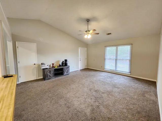 an empty room with chandelier fan and windows