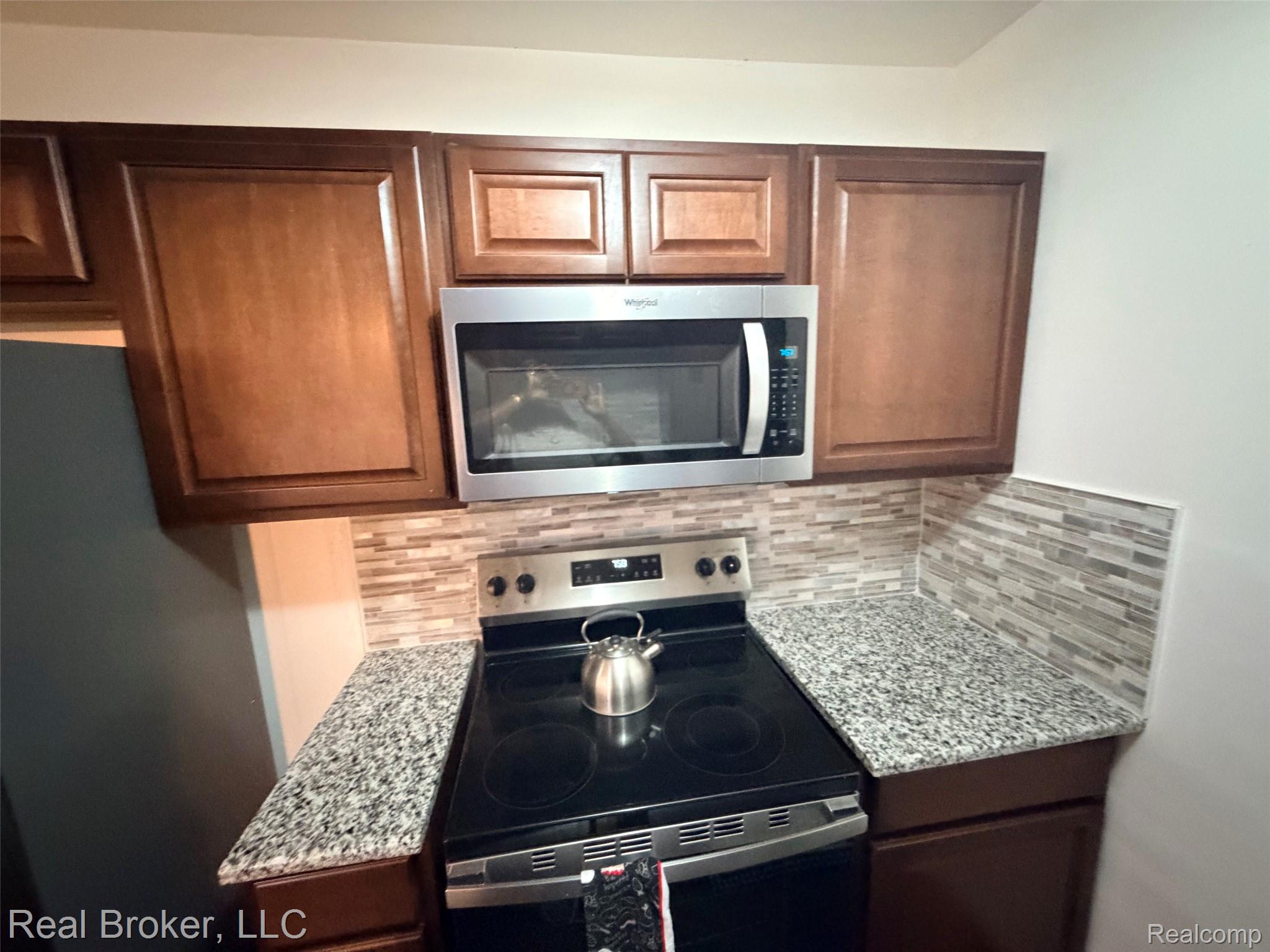 22444 Kelly Road, Unit 11 Eastpointe, MI 48021 - Photo 10 of 18 Kitchen featuring wood-finish cabinetry, speckled countertops, a tile backsplash, and a stainless steel oven with an integrated stovetop