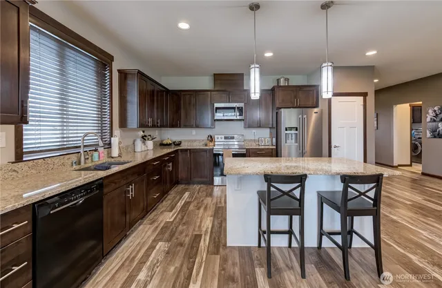 a kitchen with stainless steel appliances granite countertop wooden cabinets a refrigerator a sink a stove a dining table and chairs