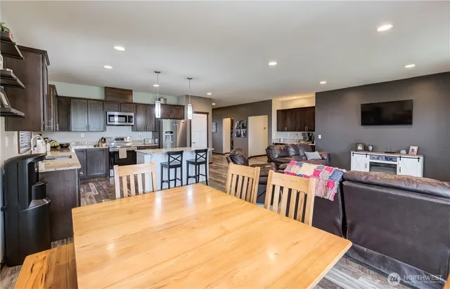 a living room with stainless steel appliances kitchen island granite countertop a dining table chairs refrigerator and a sink