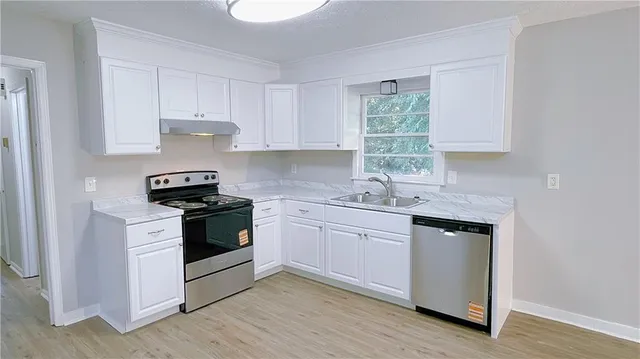 a kitchen with granite countertop white cabinets appliances a sink and a window