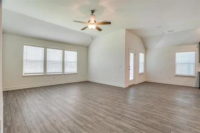 an empty room with wooden floor chandelier fan and windows