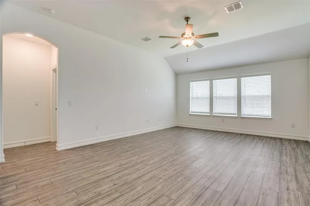 an empty room with wooden floor chandelier fan and windows