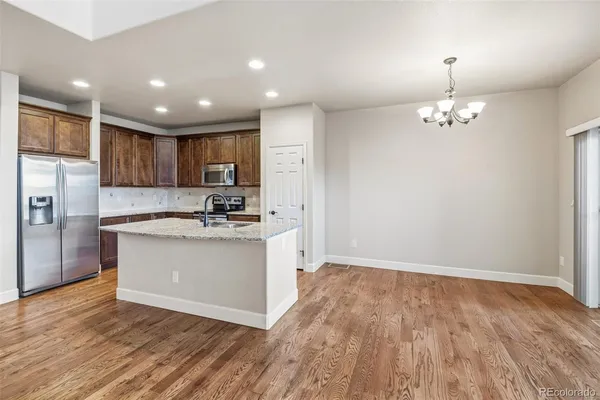 a kitchen with kitchen island granite countertop wooden floors stainless steel appliances a sink and a refrigerator