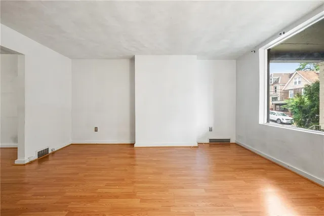 a view of an empty room with wooden floor and a window