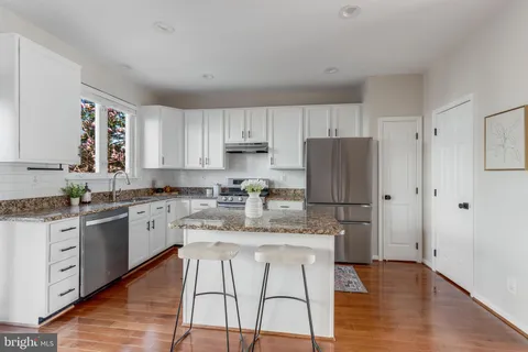 a kitchen with stainless steel appliances granite countertop a refrigerator a stove a sink and white cabinets with wooden floor