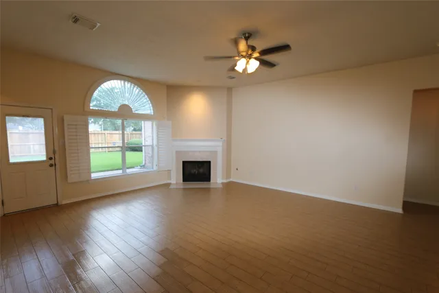 an empty room with wooden floor chandelier fan and windows