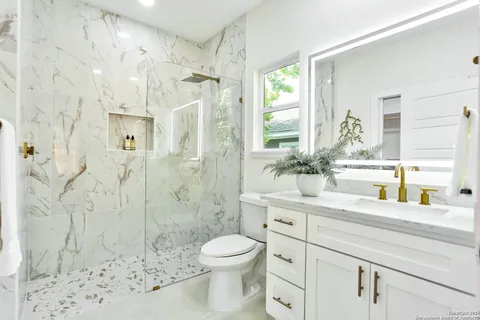 a bathroom with a granite countertop sink a toilet a mirror and shower