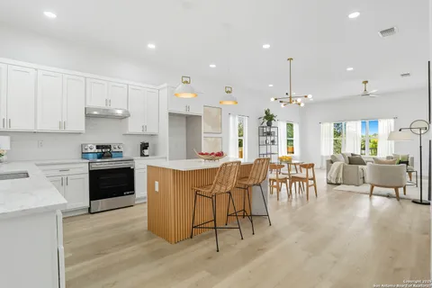 a kitchen with stainless steel appliances granite countertop a stove top oven a sink a dining table and chairs with wooden floor