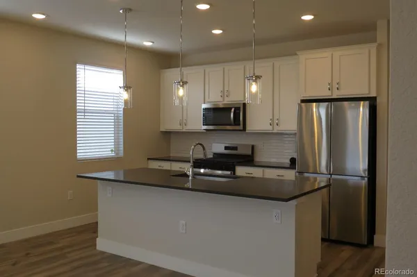 a kitchen with granite countertop a refrigerator a sink and white cabinets
