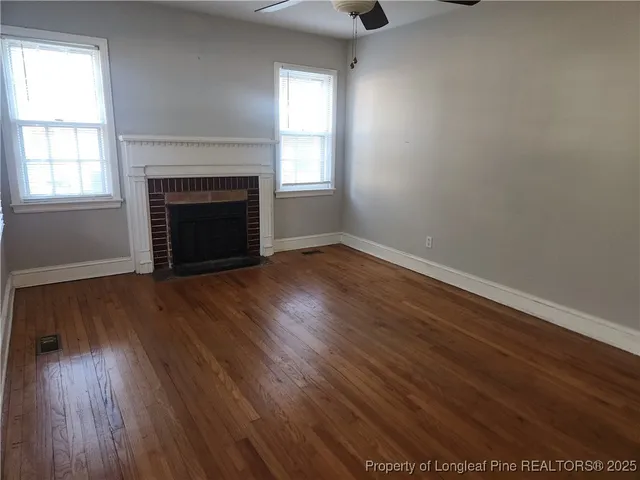 an empty room with wooden floor fireplace and windows