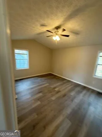 an empty room with wooden floor chandelier fan and windows