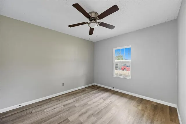 a view of an empty room with wooden floor and a ceiling fan