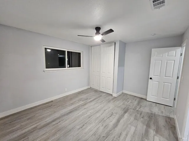 a view of an empty room with wooden floor and a ceiling fan