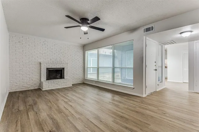 a view of an empty room with wooden floor fireplace and a window