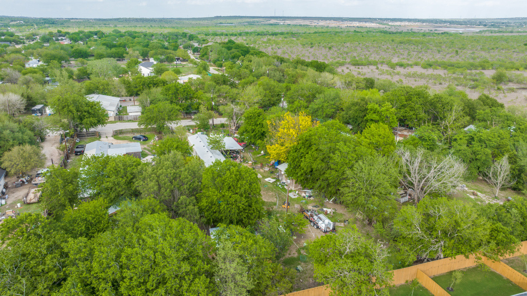 404 Quail Run Buda, TX 78610 - Photo 12 of 13 Aerial view showcasing the property nestled within a verdant landscape, surrounded by numerous mature trees and expansive undeveloped land in the distance