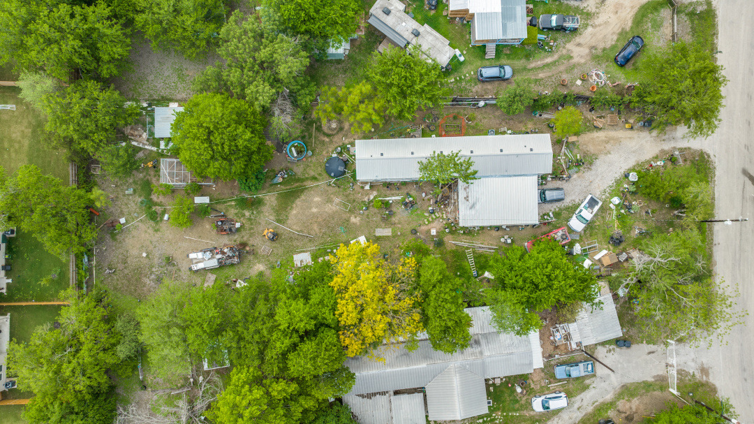 404 Quail Run Buda, TX 78610 - Photo 13 of 13 Aerial view of the property, featuring several buildings with light-colored roofs, surrounded by lush green trees and open ground