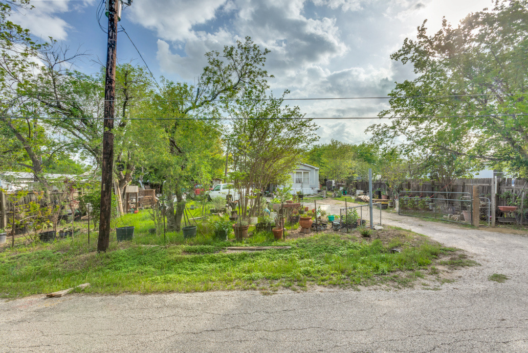 404 Quail Run Buda, TX 78610 - Photo 5 of 13 The property features a gravel driveway and a fenced yard with mature trees and various potted plants