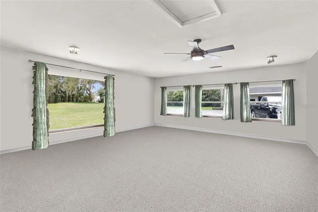 an empty room with chandelier fan and windows