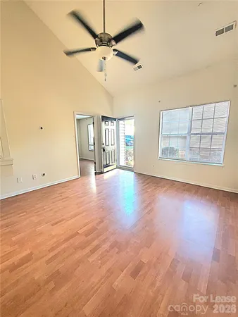 an empty room with wooden floor chandelier fan and windows