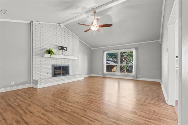 a view of an empty room with wooden floor fireplace and a window