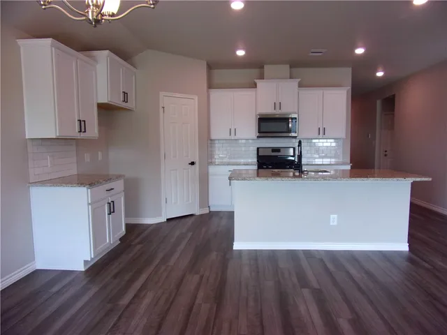 a kitchen with stainless steel appliances granite countertop a refrigerator a stove top oven a sink and dishwasher with wooden floor