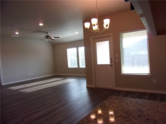 an empty room with wooden floor chandelier and windows