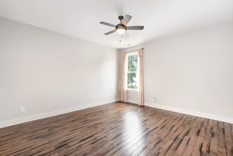 an empty room with wooden floor chandelier fan and windows