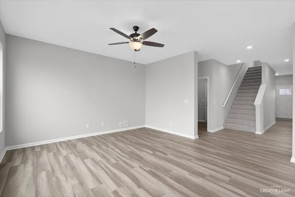 a view of an empty room with wooden floor and a ceiling fan