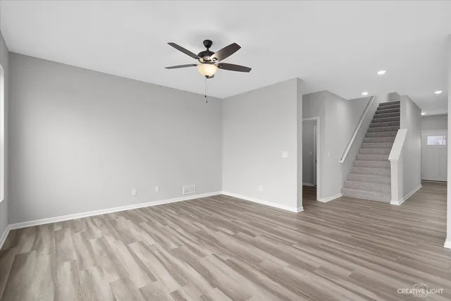 a view of an empty room with wooden floor and a ceiling fan