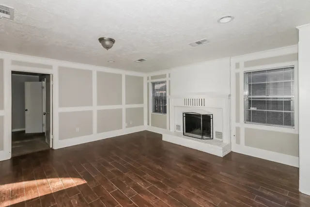 a view of an empty room with wooden floor fireplace and a window