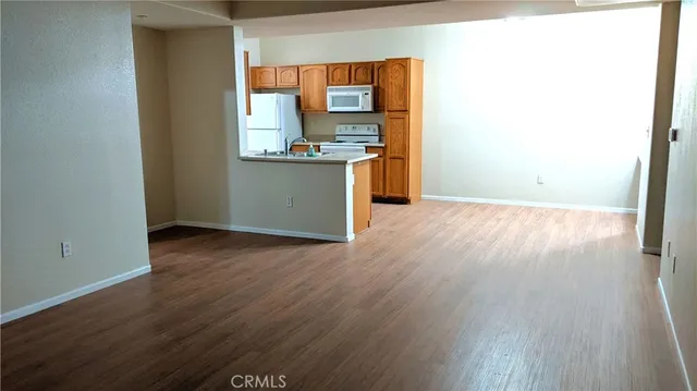 an empty room with wooden floor kitchen view and a window