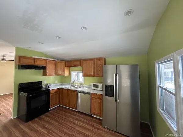 a kitchen with stainless steel appliances granite countertop a refrigerator a sink dishwasher a stove and white countertops with wooden floor