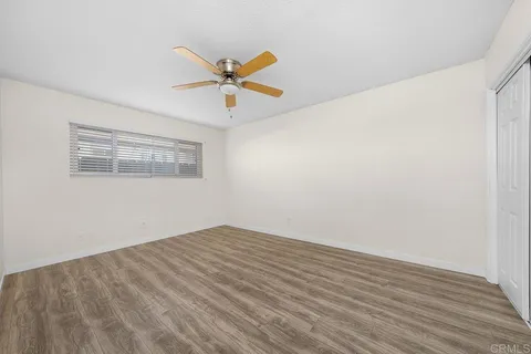 a view of empty room with wooden floor and fan