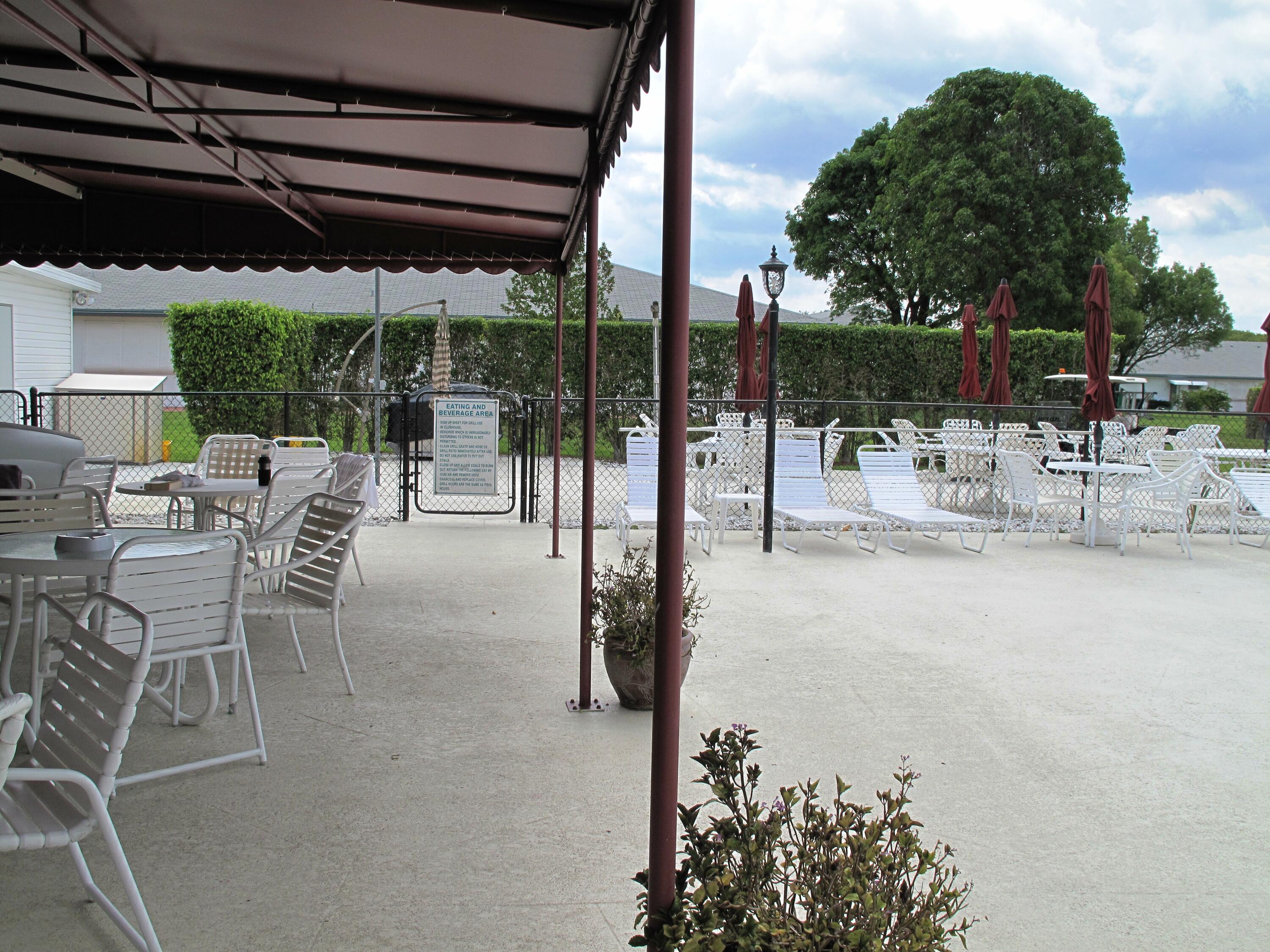 1315 High Point Way Southeast, Unit B Delray Beach, FL 33445 - Photo 35 of 41 a view of a patio with a table and chairs under an umbrella with a large tree