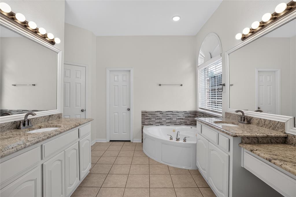 111 Ripplewood Coppell, TX 75019 - Photo 20 of 34 Bathroom featuring a corner soaking tub with mosaic tile surround, dual vanity sinks with granite countertops, and arched window with blinds